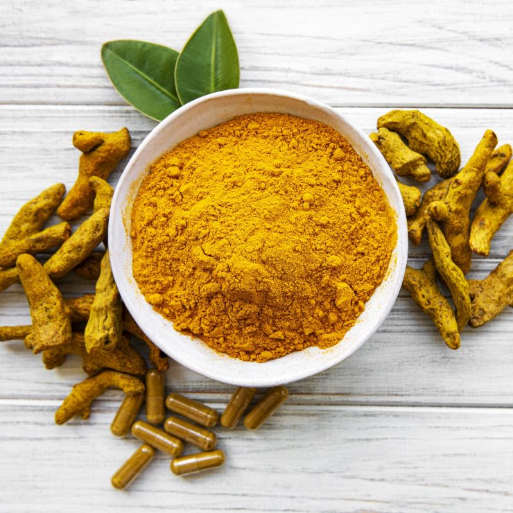 Bowl with turmeric powder and dry roots on a wooden background